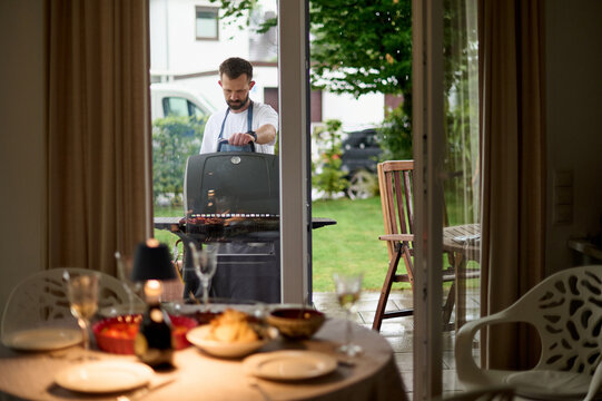 Cozy Dinner Table Set While Man Prepares BBQ Outdoors
