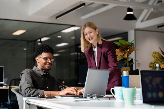 Colleagues collaborating on laptop in modern office environment