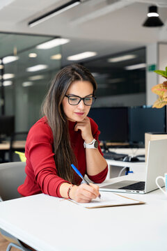 Woman working on laptop and writing notes at desk
