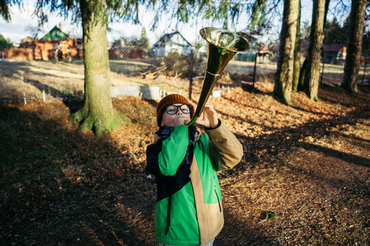 Child plays trumpet outside among trees
