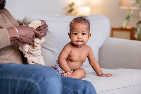 Baby on couch with parent holding clothes.