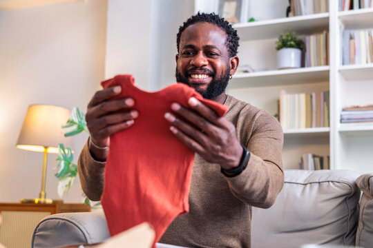 Man smiles, holding baby clothes, likely a new parent.
