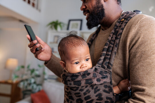 Dad with baby in carrier using phone.