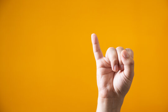 Close up of pinky finger raised on bright yellow background signifying a concept of pinky promise or small detail