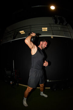 Man performs kettlebell swing in gym at night