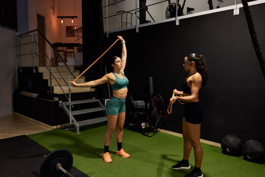 Two women stretch with resistance band in gym setting