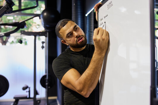 Man writing on a whiteboard in a gym setting during the day