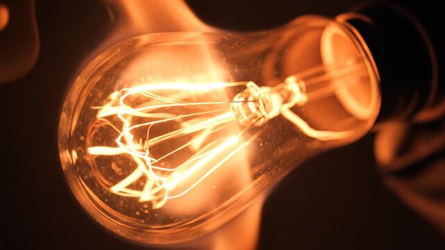 Close-up of a lit filament bulb, its glass encasing glows with a warm orange hue against a dark backdrop