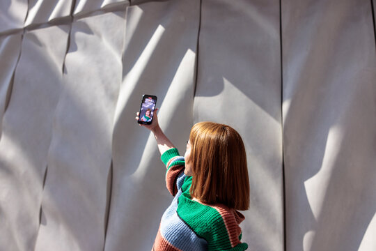 Woman records video against modern wall.