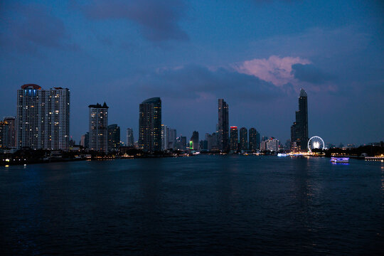 Bangkok skyline at dusk, river in foreground.