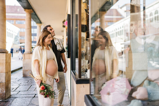 Pregnant couple window shopping for baby items in city