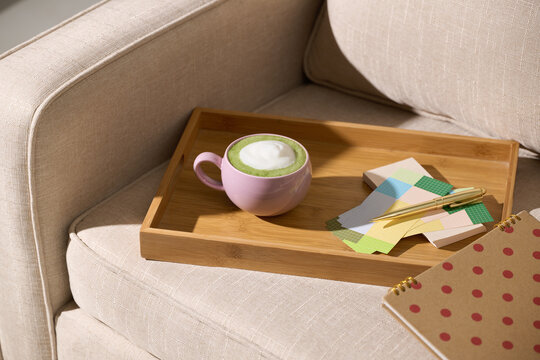 Matcha latte in a pink mug on a wooden tray with stationery