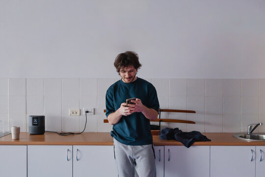 Young man checks phone while standing in modern kitchen