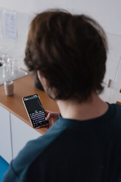 A male uses a smartphone while standing in the kitchen