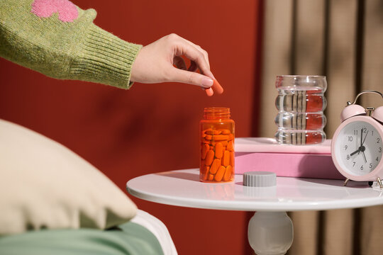 A hand takes a pill from a bottle, placed on a bedside table