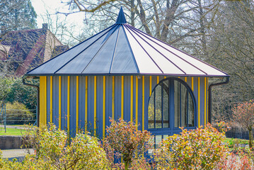 Scenic Pavilion Surrounded By Greenery And Floral Arrangements. Delightful Hexagonal Pavilion Nestled Within Lush Park Scenery