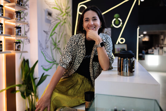 Smiling woman in cannabis dispensary with product display.