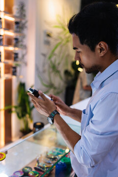 Man examines product in glass display case, using phone.