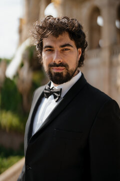 An elegant man in a black suit is looking at the camera