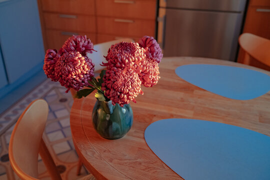 Flowers in vase on wooden kitchen table at sunset