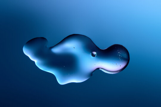 Droplet of fluid gel on dark purple and blue gradient backdrop.