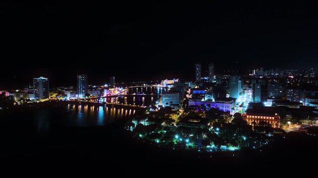 Aerial night view of the city of Recife, Pernambuco, Brazil, highlighting the illuminated urban center and the Pal&aacute;cio do Campo das Princesas along the river. 
