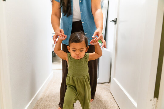 Child Learns to Walk in a Hallway With Support From an Adult