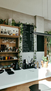 Modern cozy coffee shop interior with bar counter, shelves, menu board and indoor plants. Calm urban atmosphere with vintage tones and film grain, soft natural light