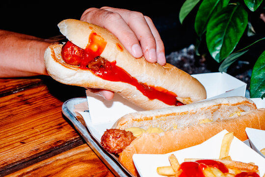 a man lifts a hot dog from a tray, dripping with ketchup