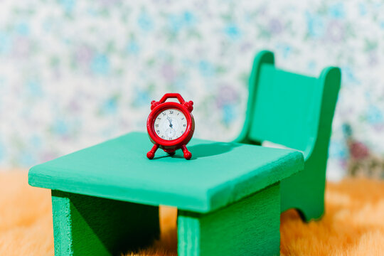 a tiny red alarm clock on a small green wooden table