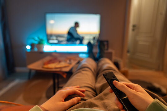 Person holding remote while watching TV on sofa