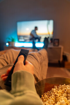 Hand holding remote control while watching TV with popcorn