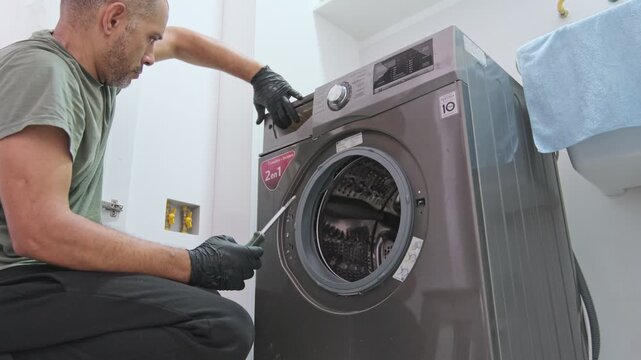 Male technician with gloves working on a broken laundry appliance, unscrewing the top panel