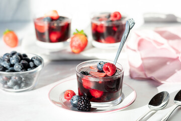 A homemade mixed berry jelly cup topped with fresh berries in bright sunlight.