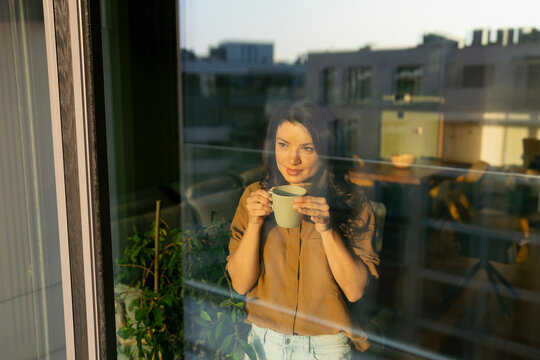 Woman drinks coffee by window
