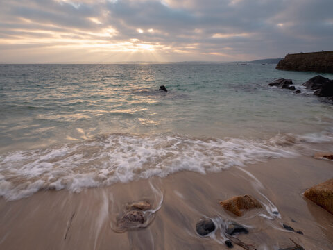 Sunsrise over a calm beach with rocks and breakwater
