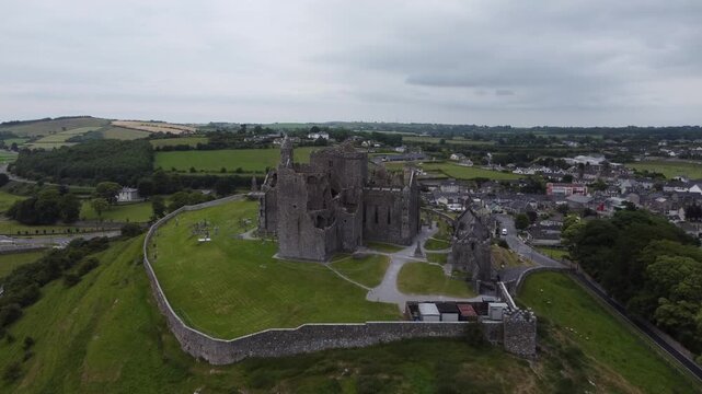 Medieval fortress ruins on a grassy mound under a cloudy sky.