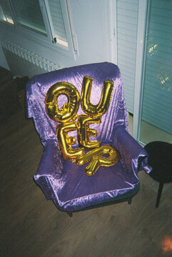 foil balloons spelling the word queer on a velvet armchair, 35mm film