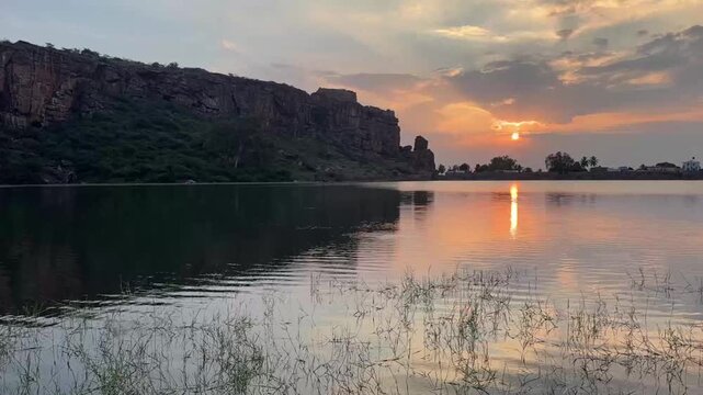 A slow-motion time-lapse of sunset clouds and lake waters, with the stunning Badami red sandstone caves in view.