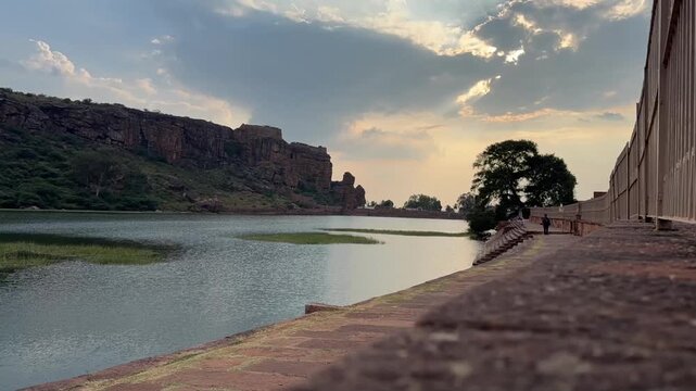 A stunning time-lapse of Agastya Lake, with its calm waters reflecting the towering red sandstone cliffs of Badami&rsquo;s rock-cut caves, capturing the serene beauty and majestic landscape
