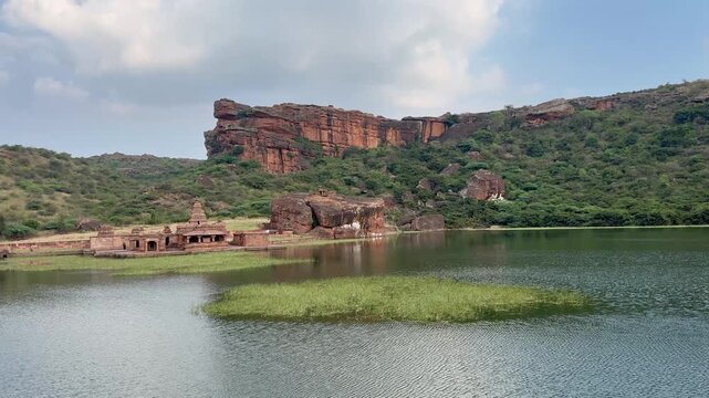 A breathtaking panoramic view of Agastya Lake with the Bhoothnath Temple at its edge, set against the massive red sandstone cliffs at the back, capturing the serene and majestic landscape of Badami