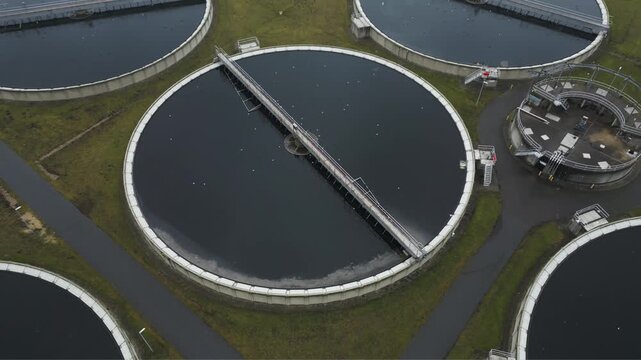 Top down drone view of circular wastewater clarification basins with rotating treatment arms and dark water surfaces.