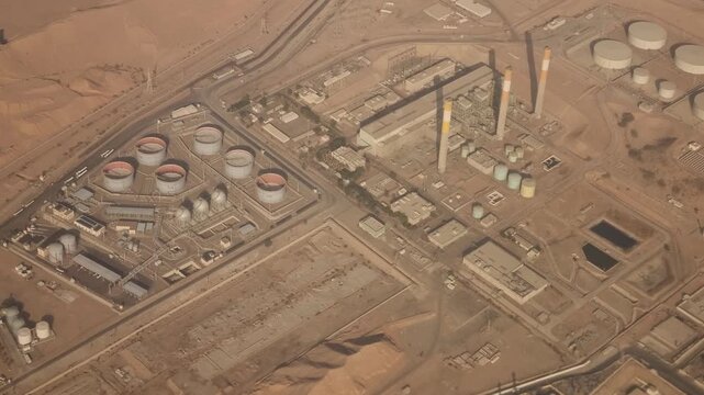 Aerial view from an airplane over Jordan showing a large industrial complex in the desert, likely an oil refinery or gas processing plant, with storage tanks, pipelines, and tall chimneys