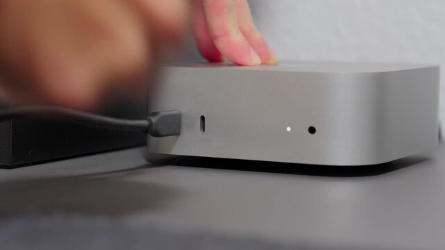 Close-up of a hand plugging a black usb-c cable into the port of a silver aluminum computer.