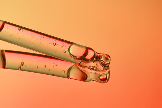 Clear glass pipette with hydrting face serum on orange background.