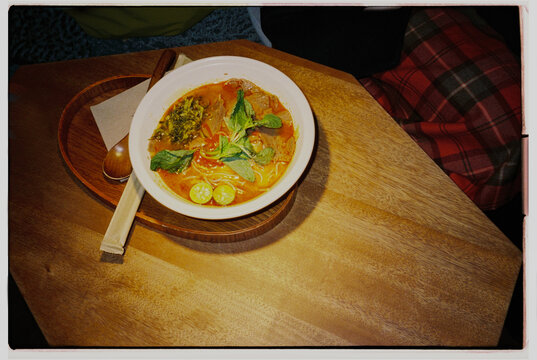 Bowl of soup with herbs and lime on a wooden table 