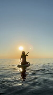 Young woman walking on stand up paddle sup boards by the sea during summer vacation. Beautiful girl flat water paddling against sea and sky background. Slow motion