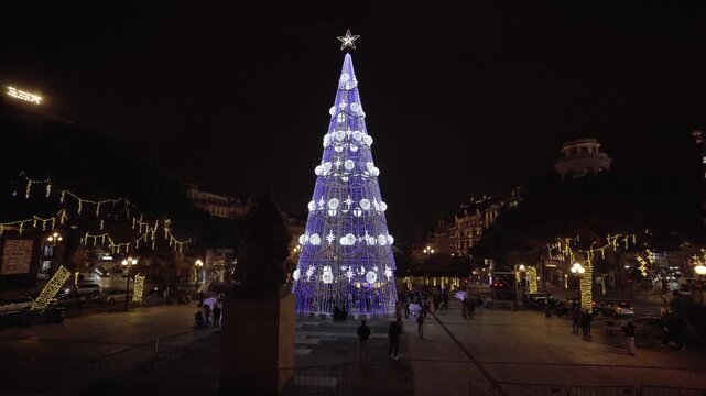 Tall blue and white illuminated Christmas tree in the city center.