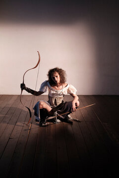 Model poses with bow and arrow in indoor setting during shoot