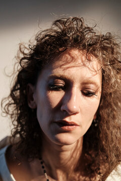 Woman with curly hair looks downward in soft light